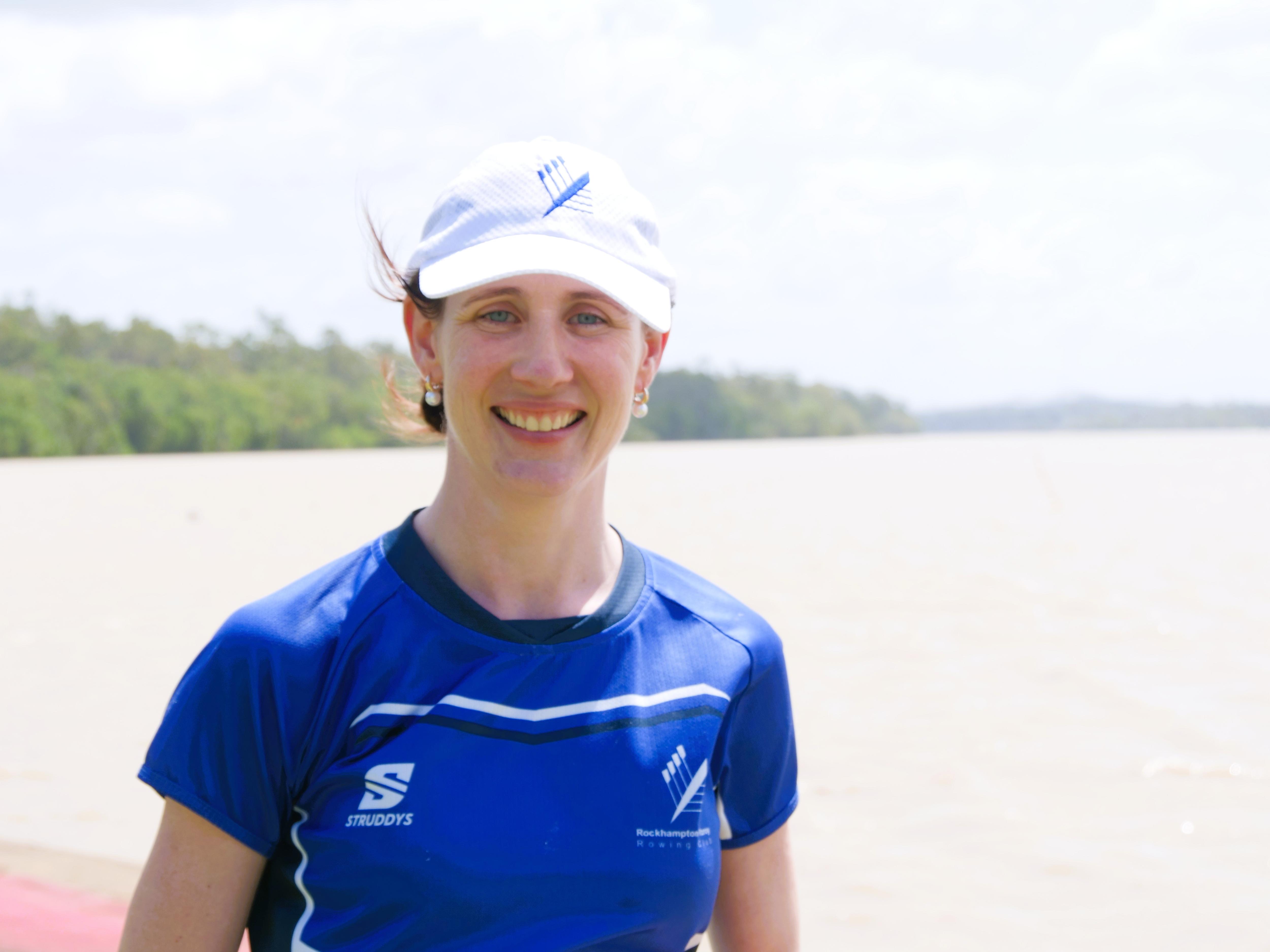 A woman wearing a white cap and blue shirt standing at a river.