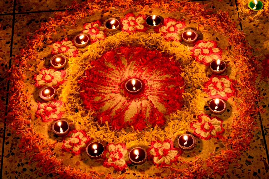 Intricate design of colourful powders, flowers and rice laid out on floor.