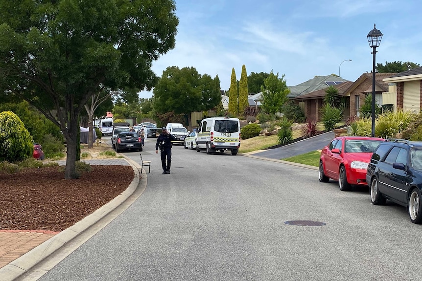 A police officer walking on a street with a police car and van