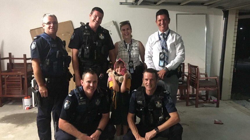 A photograph of five year old Alyssa Jayde New with six police officers in a garage.