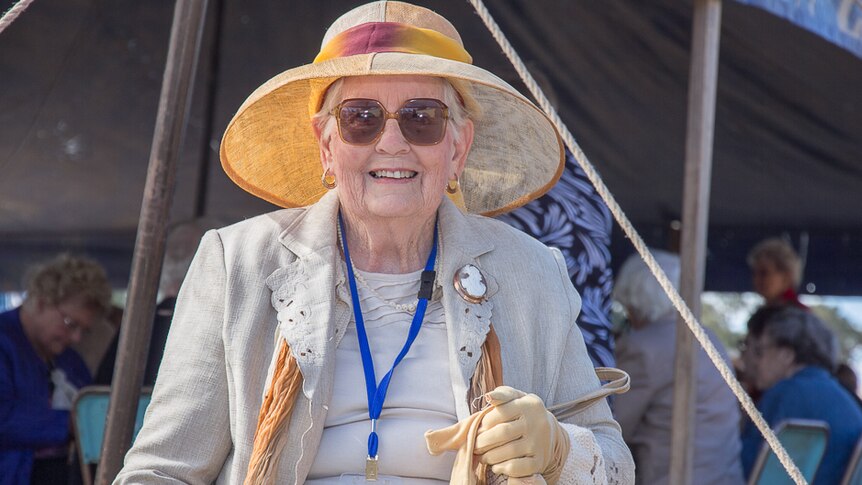 An older woman in hat, handbag and gloves in front of a tent