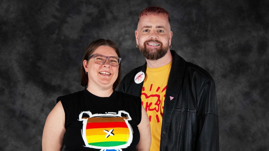 A woman and a man pose in front of a grey backdrop, smiling at the camera. 