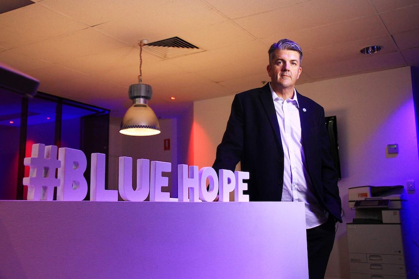 Blue Hope director Mark Kelly stands in signage in an office.