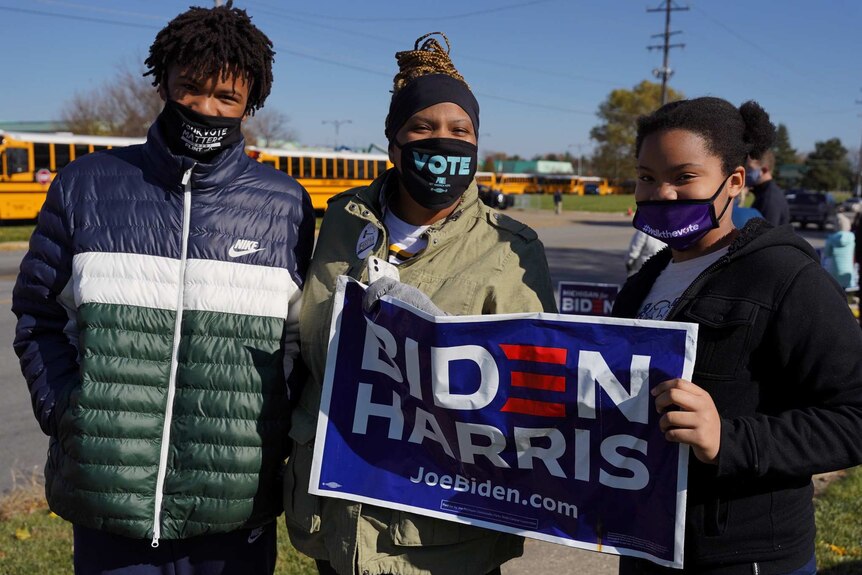 A woman with a teenage boy and teen girl holding a 'Biden Harris' sign
