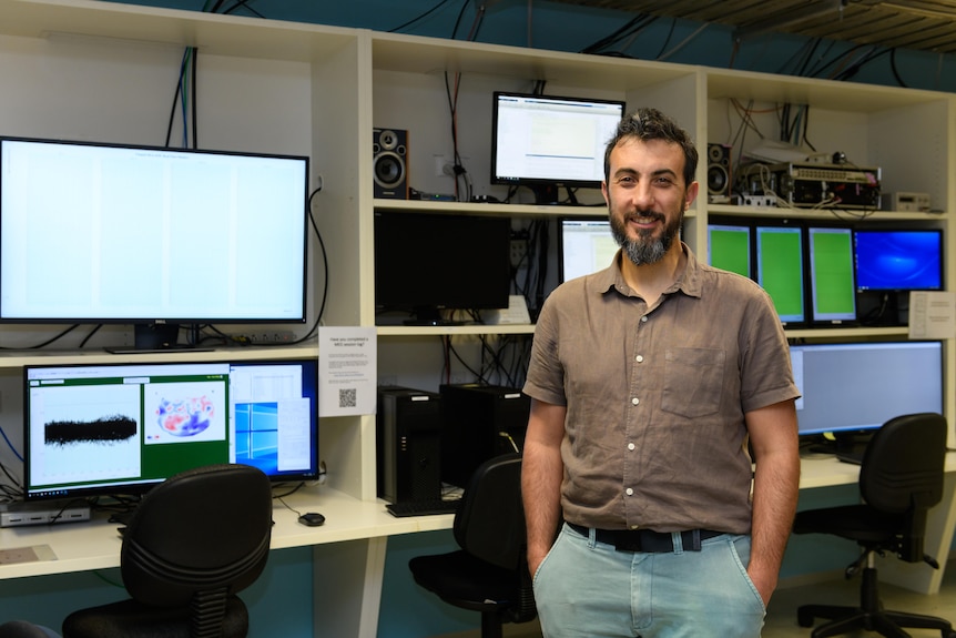 Photo of a man standing in front of a series of computers.