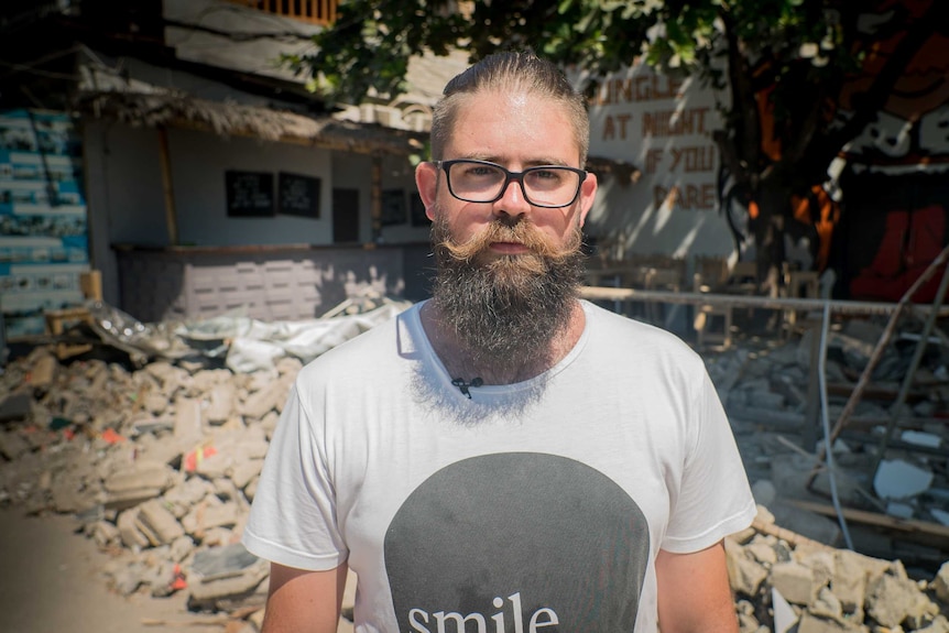 Brendan Muir stands in front of a ruined building