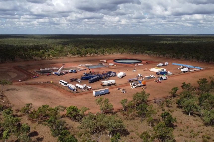 An aerial shot of a drilling site in the Beetaloo Basin. Machinery and vehicles are in a land clearing surrounded by trees,