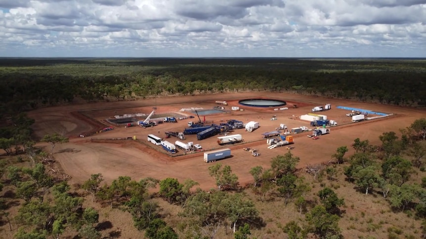 An aerial shot of a drilling site in the Beetaloo Basin. Machinery and vehicles are in a land clearing surrounded by trees,