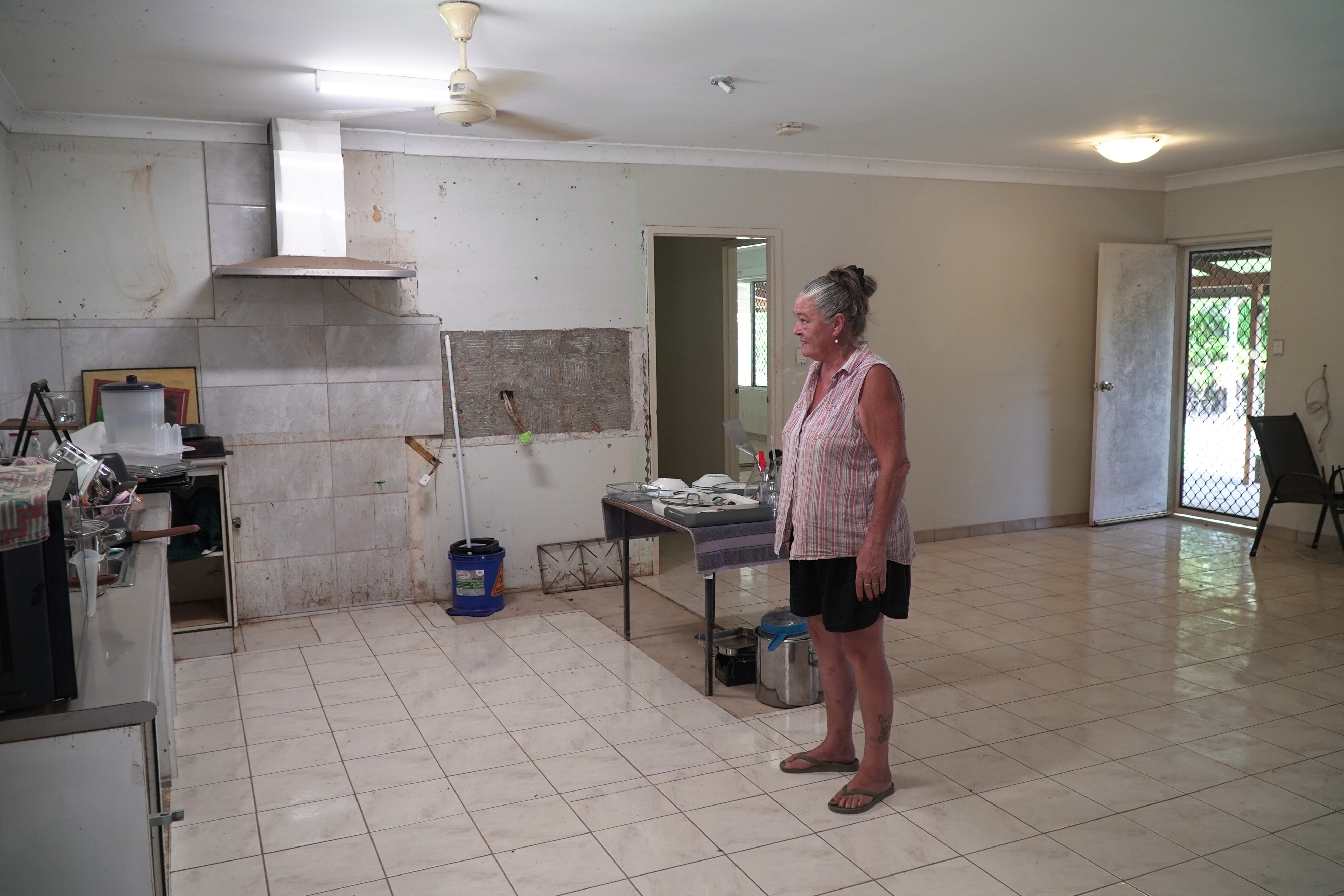 A woman stands in a flood damaged kitchen.