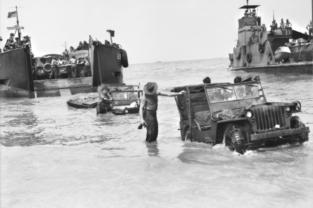 Black and white image from Australian War Memorial of landing craft delivering jeeps and troops ashore during World War II