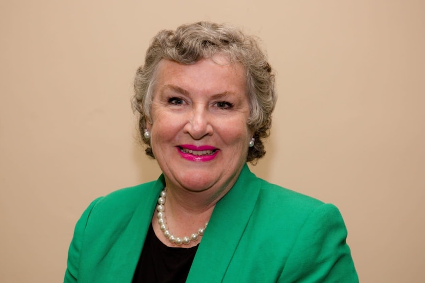 A woman smiles at the camera in front of a plain background