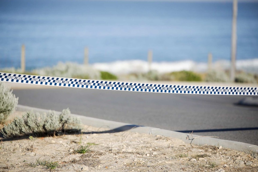A picture of police tape strung across a road in front of a beach.