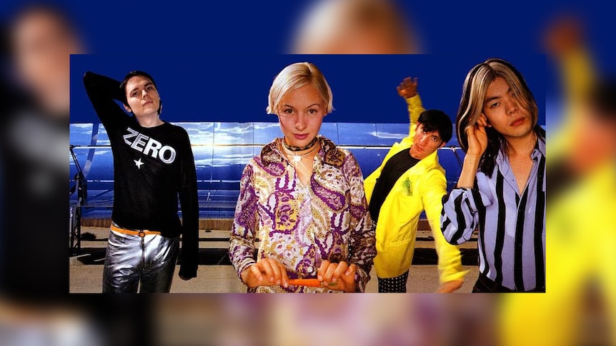 Four young people strike strange poses at a solar farm.