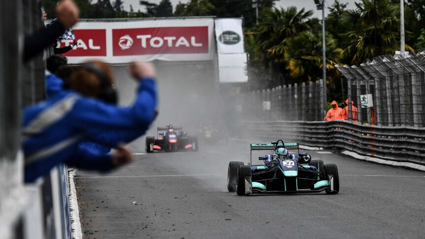 Billy Monger crosses the line in a single-seater race car with spray behind him
