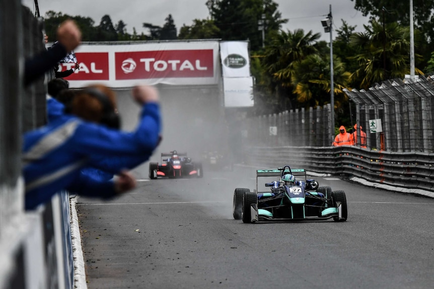 Billy Monger crosses the line in a single-seater race car with spray behind him