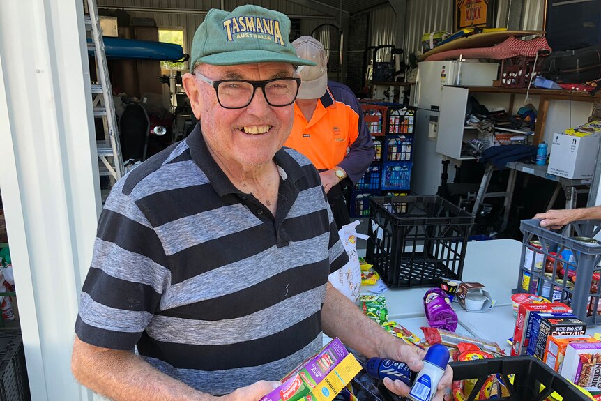 A man in a green hat packs groceries into a milk crate.