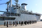 A ship at dock, with a parade of naval personnel marching in fornt