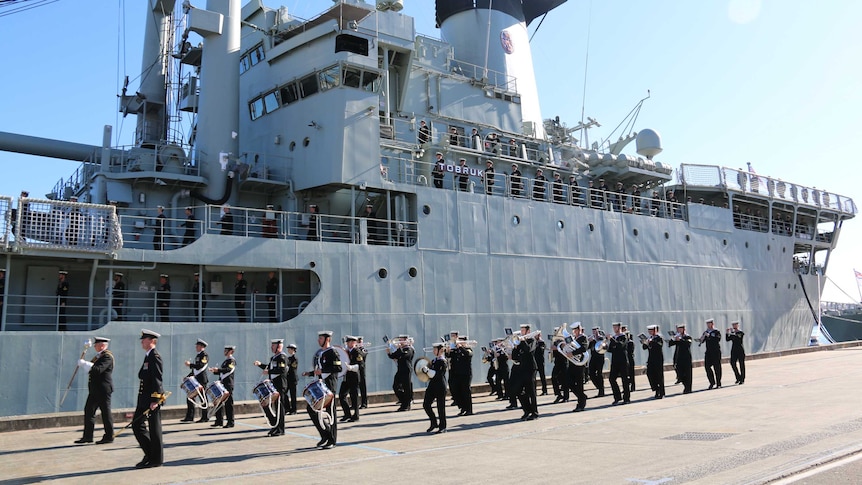 A ship at dock, with a parade of naval personnel marching in fornt