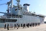 A ship at dock, with a parade of naval personnel marching in fornt