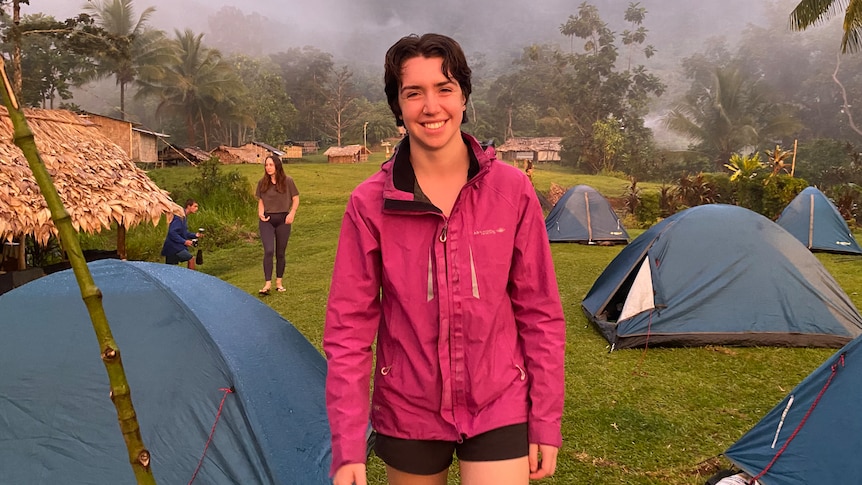 A young woman wearing hiking gear stands in a misty field amongst small tents. 