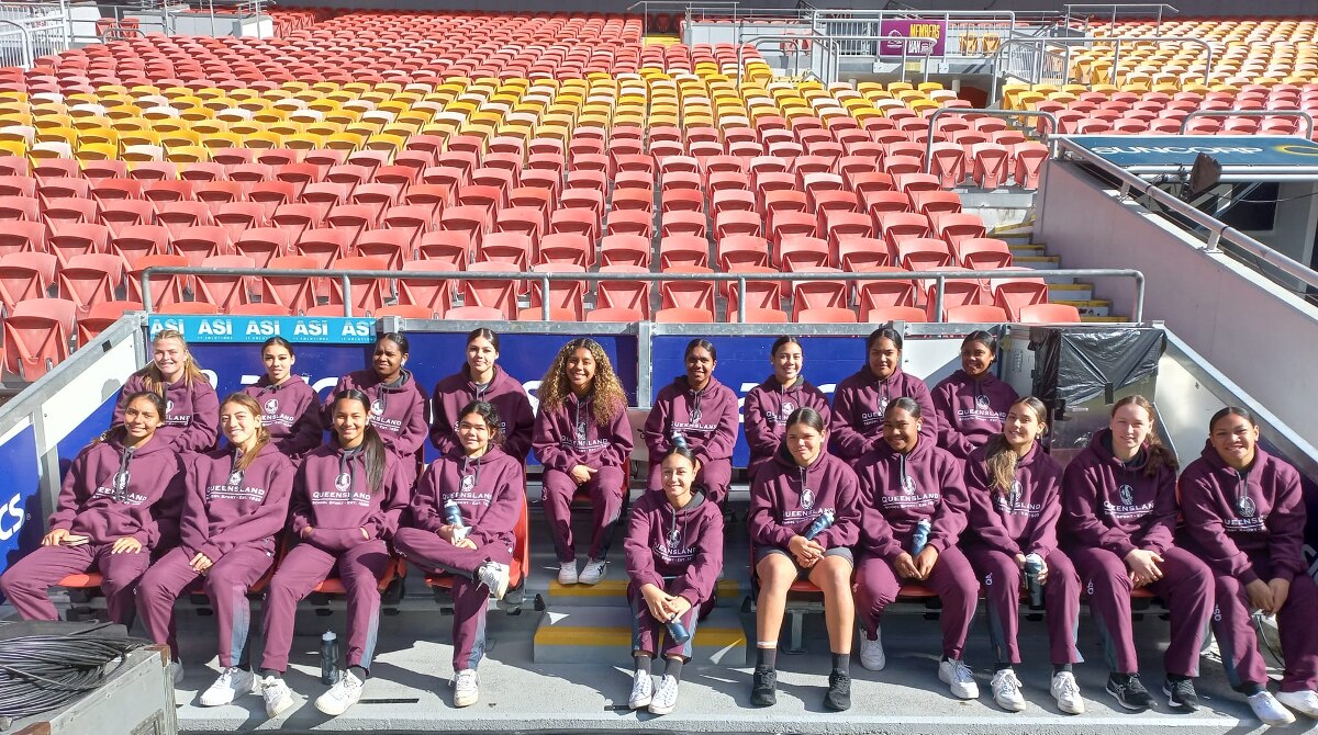 Group of girls in maroon tracksuits sitting in a stadium smiling