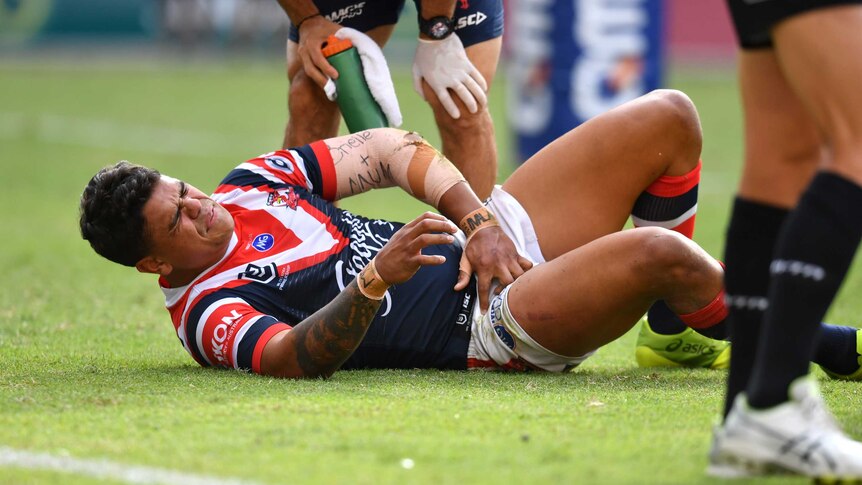 Latrell Mitchell holds his hand to his groin with a grimace on his face lying on the floor