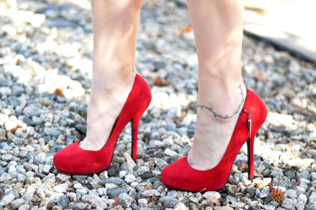 A woman wearing red stiletto high heel shoes standing on gravel.