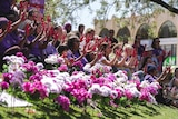 a crowd of people showing red painted hands behind flowers