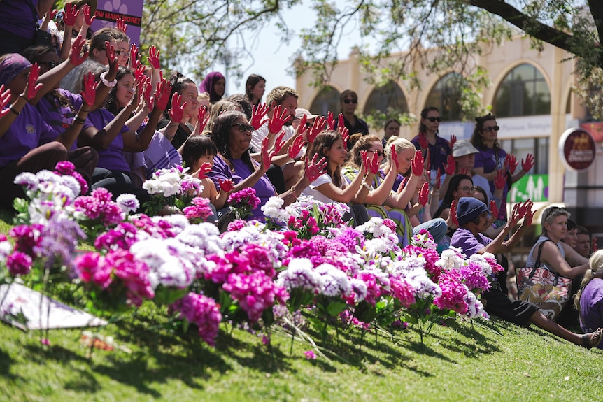 a crowd of people showing red painted hands behind flowers