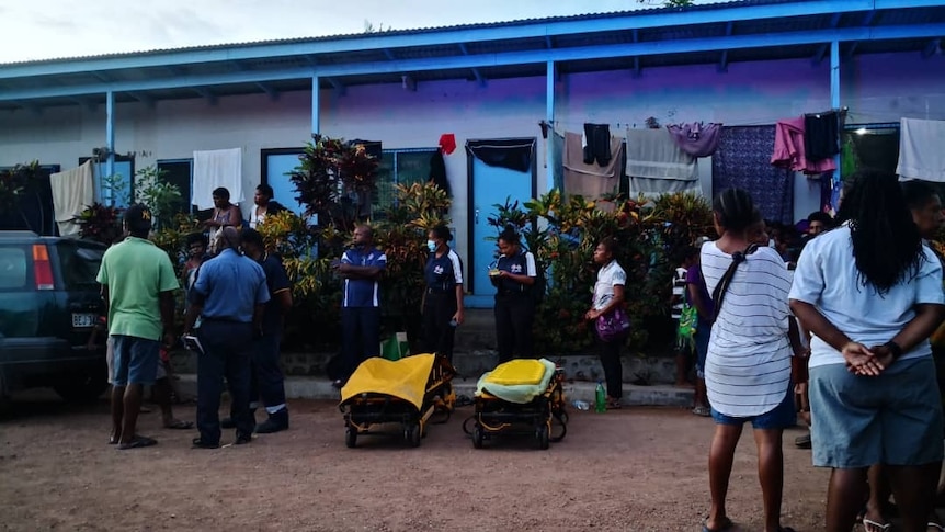 You view two low yellow hospital stretchers in the middle of a crowd on a dirt road.