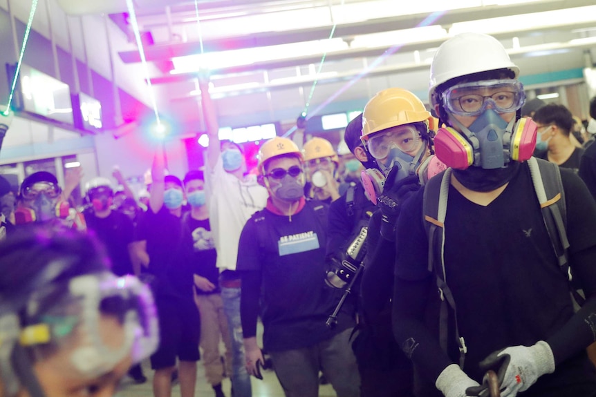 A group of Hong Kong protesters in tear gas masks, hard hats and gloves, wielding lasers