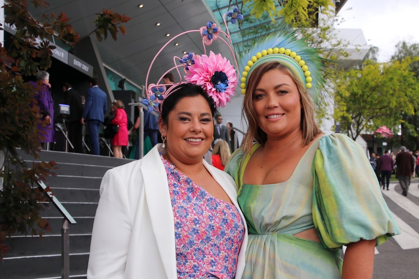 Two women in brightly coloured outfits smile and stand beside one another.