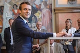Emmanuel Macron places his vote into a box.