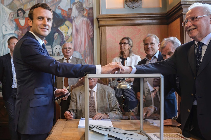 Emmanuel Macron places his vote into a box.