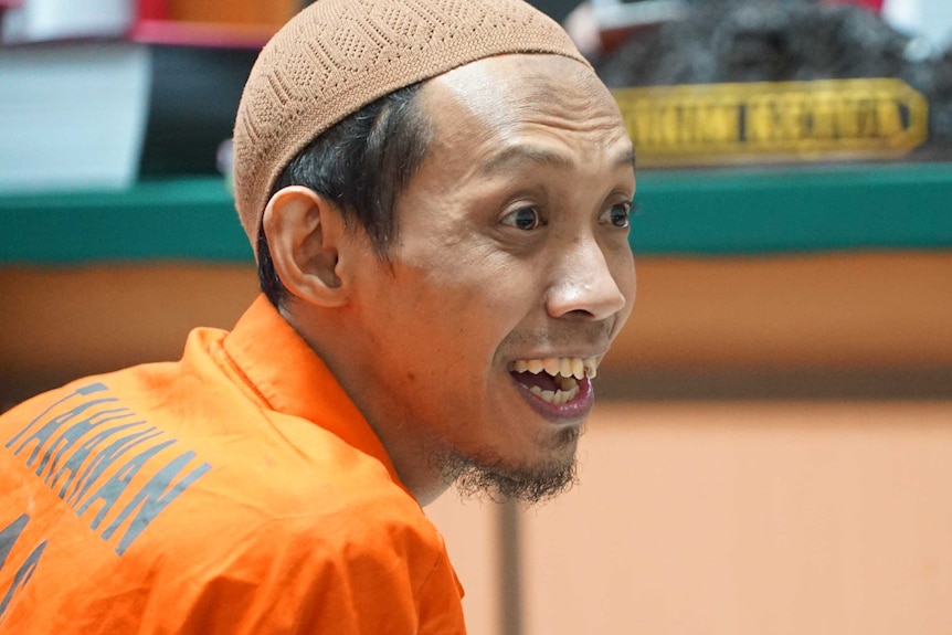 A man wearing an orange prison uniform with a surprises, happy expression on his face.