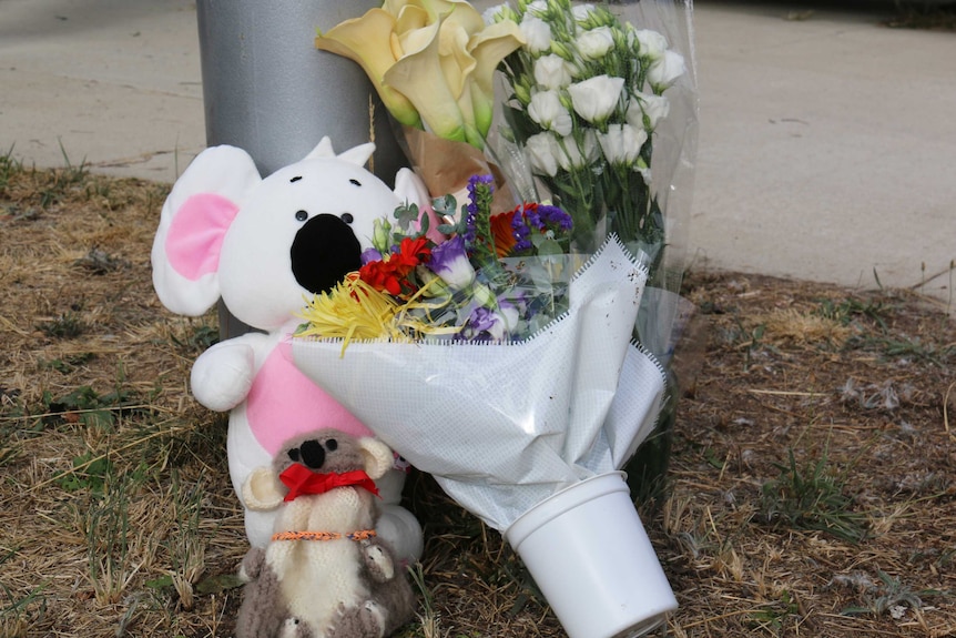 Two teddy bears and some flowers outside the fenced-off house.