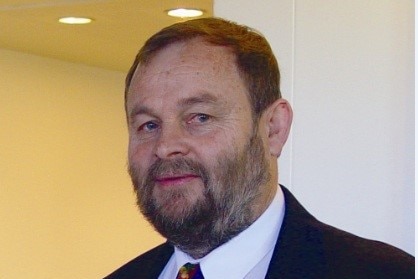 A man with a beard wearing a dark suit looks at the camera