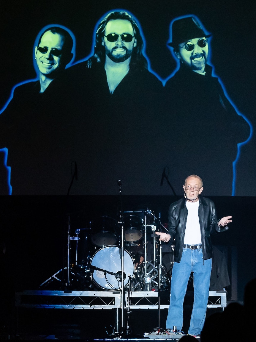 man standing on a stage in front of image of Bee Gees 