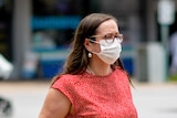 A woman wearing a face mask walks across a road in the Darwin CBD.
