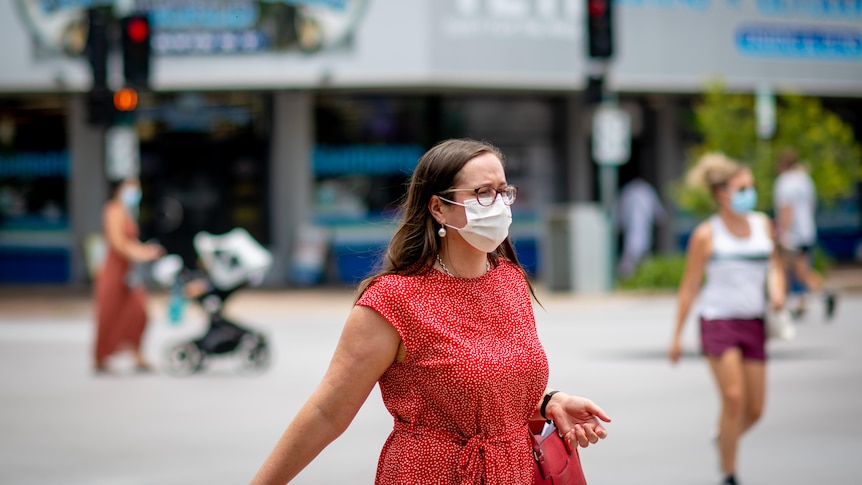 A woman wearing a face mask walks across a road in the Darwin CBD.