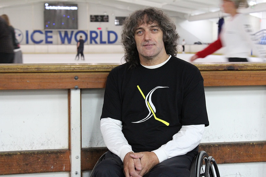 Darren Belling sitting in a wheel chair in front of an ice skating rink.