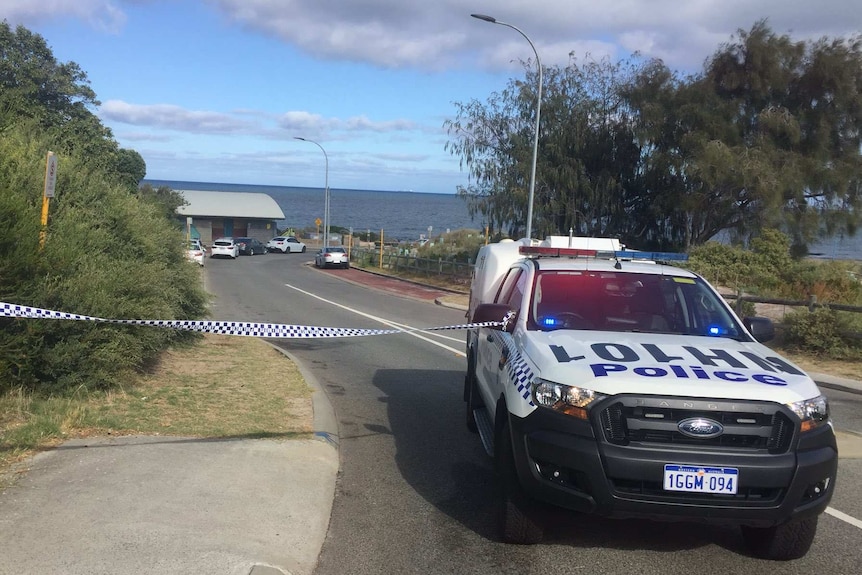 .A police car and tape blocks road access to Trigg Beach, which is visible in the background.