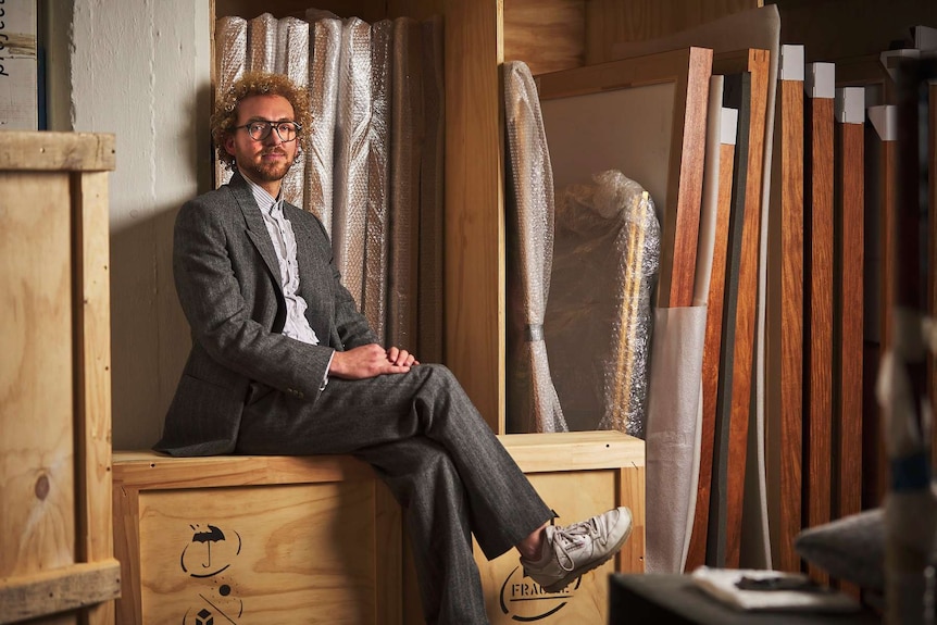 Gallery owner Michael Bugelli sits on a wooden box in a warehouse.