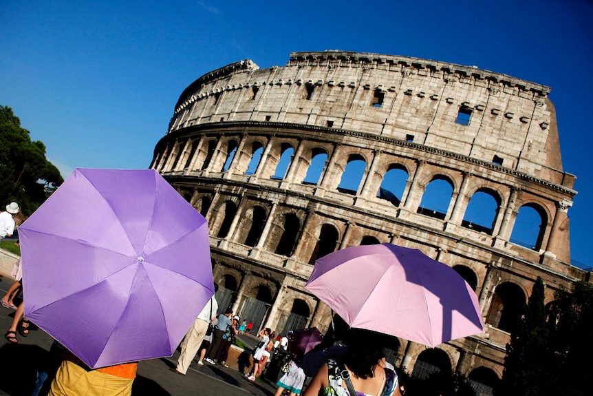 Tourists use umbrellas to shade themselves from the sun as they visit Rome's ancient Colosseum