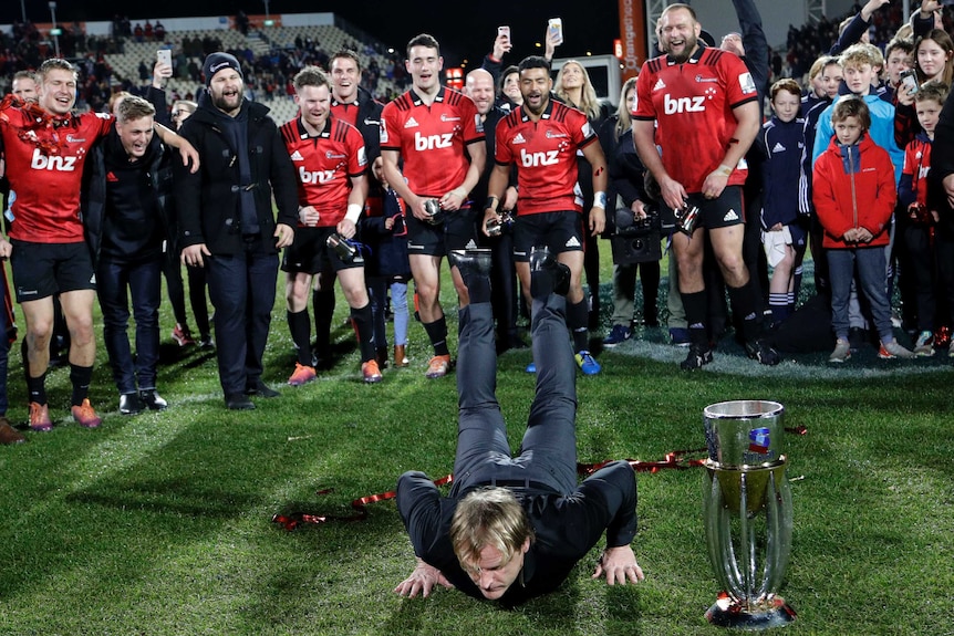 A man lies on the ground with his torso next to a trophy as he breakdances after his rugby union team won.
