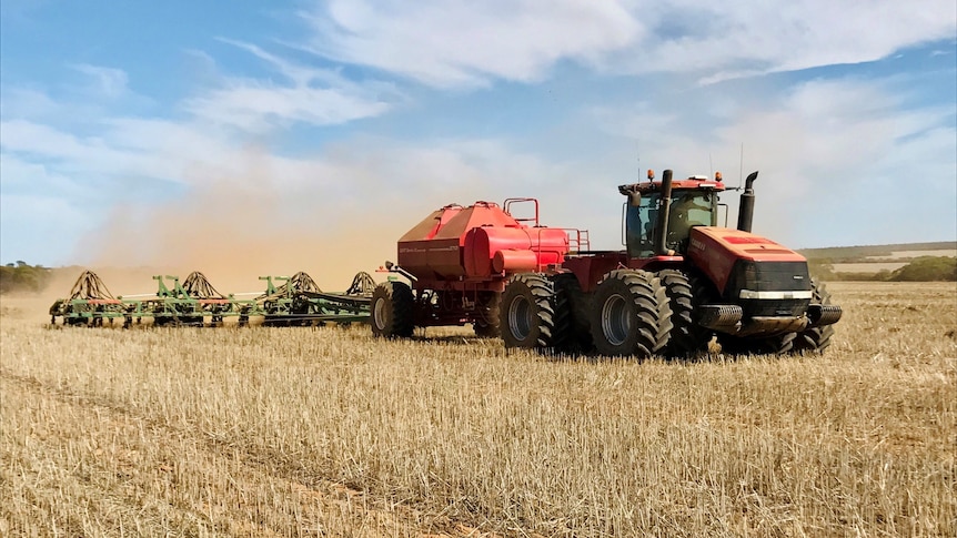 A tractor pulls a seeding rig, kicking up dust
