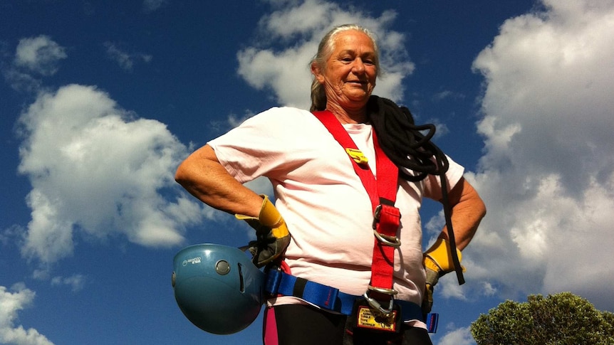 A woman with grey hair wears abseiling equipment