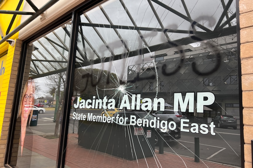 a photo of a window with "jacinta allan mp" on it is smashed and spraypainted
