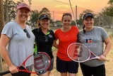 Four women holding tennis racquets in front of tennis court.