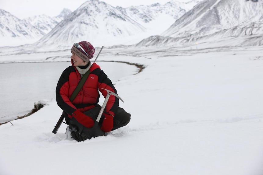 Image of heidi crouching doing on the ice in the Arctic surrounded by snowy hills and mountains